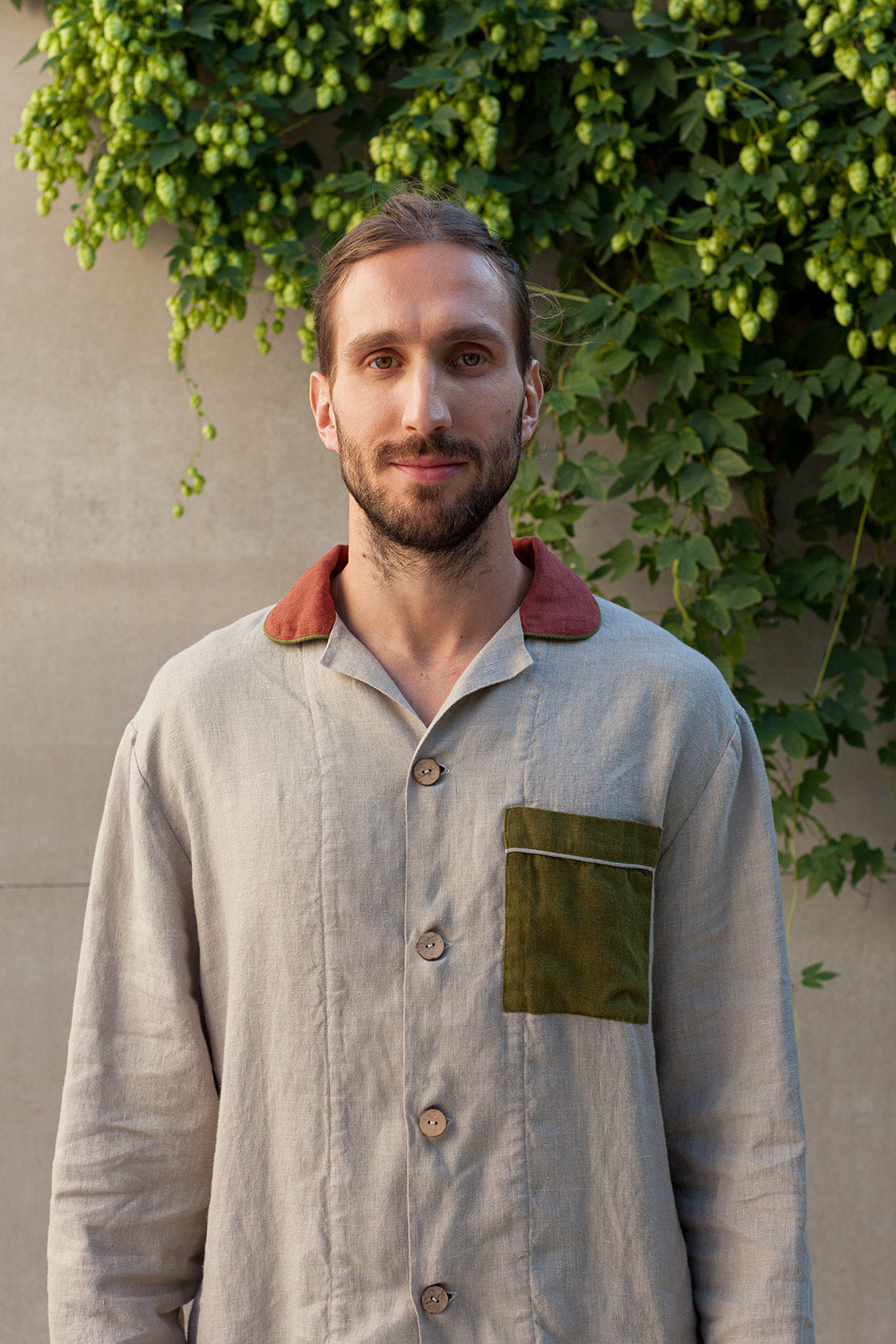 A man standing outdoors wearing a gray linen pyjama set with a collar, pockets.